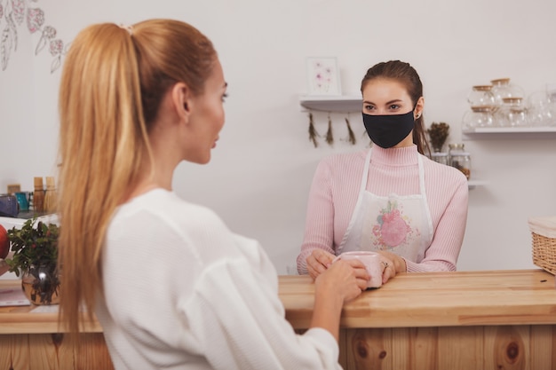 Frau kauft Kaffee während des Coronavirus-Pandemie-Barista, der medizinische Maske trägt