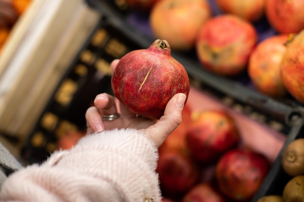 Frau kauft rote reife Granatäpfel in ihren Händen auf dem örtlichen Obstmarkt der Bauern 39. Der Käufer am Obstregal wählt sie aus und legt sie in eine wiederverwendbare Zitrusfrüchte-Diät