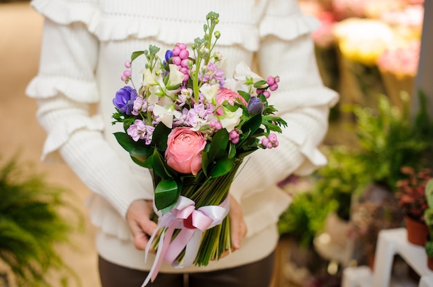 Frau kleidete in einer weißen Strickjacke an, die einen hübschen Blumenblumenstrauß hält