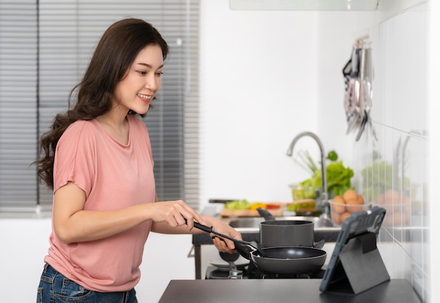 Frau kocht und bereitet Speisen nach einem Rezept auf einem Tablet-Computer in der Küche zu Hause zu