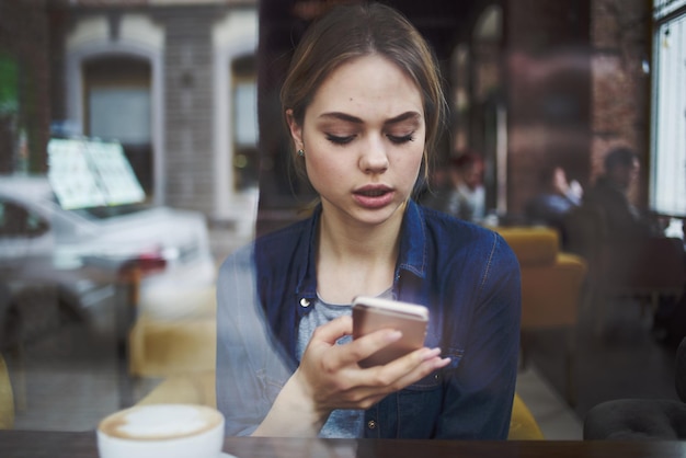 Frau kommuniziert am Telefon eines Cafés am Tisch mit einer Tasse Kaffee im morgendlichen Lebensstil