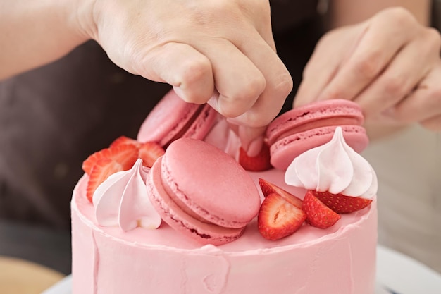 Frau Konditor dekoriert rosa Kuchen mit Makronen und Beeren Nahaufnahme Kuchenherstellungsprozess Selektiver Fokus