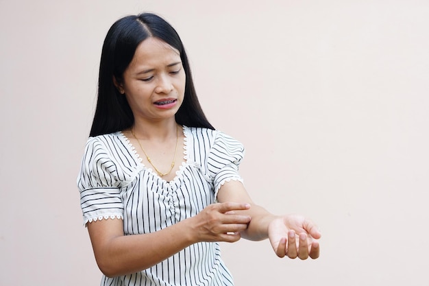 Frau kratzt sich am Arm vor Juckreiz auf hellgrauem Hintergrund Ursache für juckende Haut sind Insektenstiche