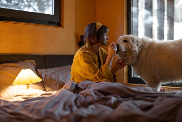 Frau kümmert sich um ihren Hund, während sie im Bett in einem winzigen Schlafzimmer einer Holzhütte in der Natur liegt