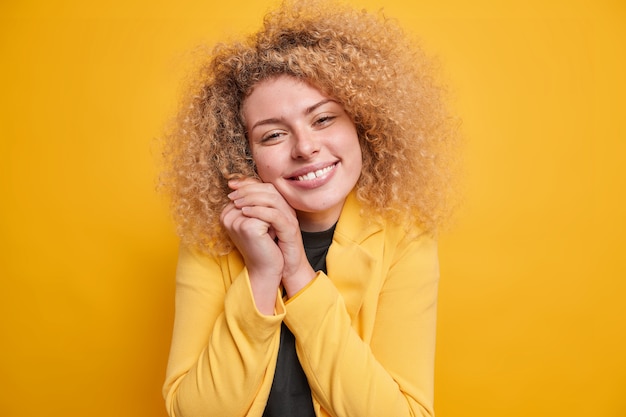 Frau lächelt sanft hält die Hände in der Nähe des Gesichts gute Laune drückt positive Emotionen aus trägt formelle Jacke