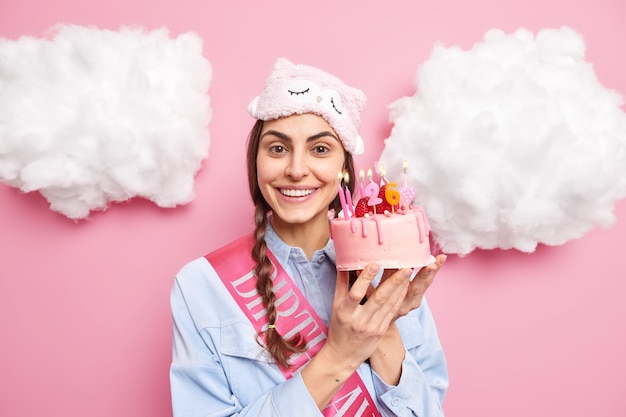 Frau lächelt sanft hält köstlichen Kuchen feiert Geburtstag in lässiger Hauskleidung isoliert auf Rosa