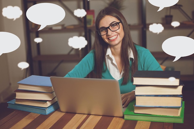 Frau lächelt Sie arbeitet mit vielen Büchern und Laptop am Tisch