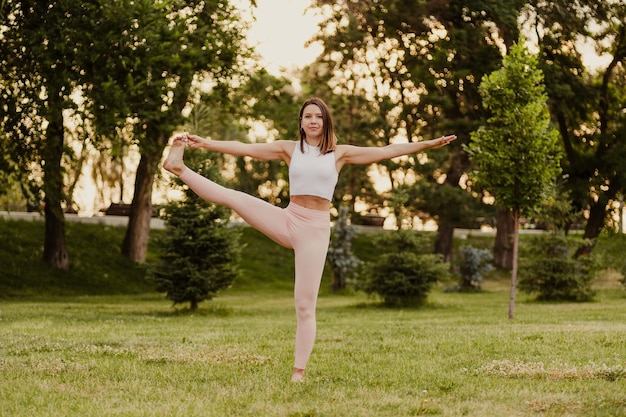 Frau lächelt und balanciert auf einem Fuß Schöne junge Frau, die Utthita Hasta Padangusthasana Yoga Asana in der Natur praktiziert