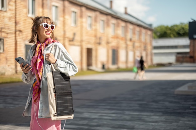 Frau lädt Telefon von tragbarem Solarpanel auf, während sie im Freien spazieren geht