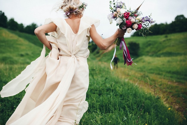 Frau läuft mit dem Hochzeitskleid und einem Blumenstrauß