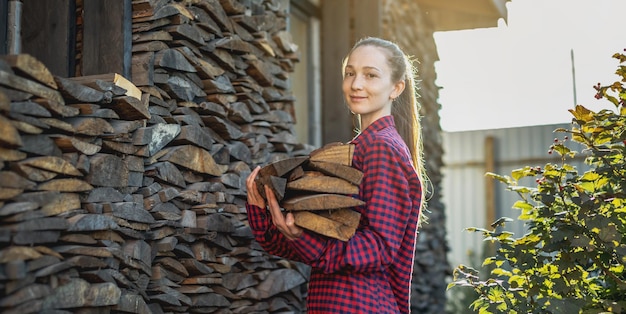 Frau legt Holz aus einem Holzhaufen für einen Heimkamin in die Hände Holzbefeuerte Heizung und die Energiekrise