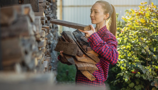 Frau legt Holz aus einem Holzhaufen für einen Heimkamin in die Hände Holzbefeuerte Heizung und die Energiekrise