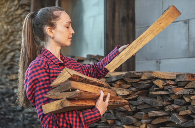 Frau legt Holz aus einem Holzhaufen für einen Heimkamin in die Hände Holzbefeuerte Heizung und die Energiekrise