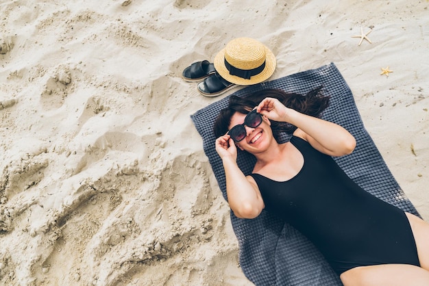 Frau legt sich im Badeanzug auf eine Decke auf Sand