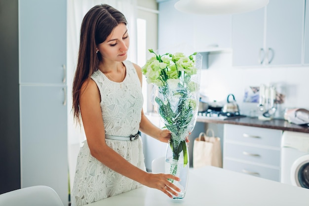 Frau legt Strauß Eustoma-Blumen auf den Tisch Hausfrau genießt Dekor und Interieur der Küche