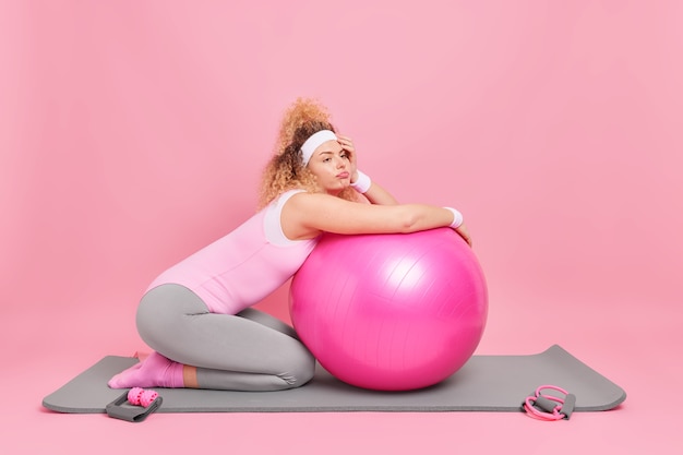 Frau lehnt sich an Fitnessball ruht, nachdem die Trainingseinheit in Activewear gekleidet ist, macht eine Pause von den Trainingsposen auf Karemat