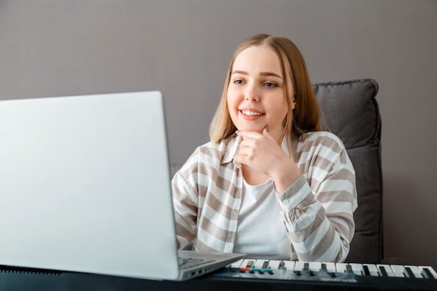 Frau lernt mit Laptop online Klavier zu spielen. Frau spielt Tasteninstrument auf Synthesizer-Klavier während des Online-Unterrichts mit dem Lehrer. Online-Konzert-Stream-Performer für Online-Publikum im Laptop.