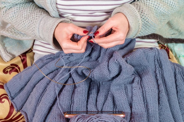 Foto frau lernt stricken und schaut auf ihr smartphone, nahaufnahme