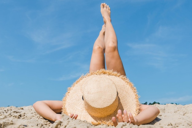 Frau liegt am Sandstrand und überkreuzt die Beine im Sommerurlaub