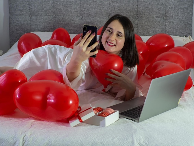 Frau liegt auf dem Bett mit roten Luftballons für die Valentinstagsparty