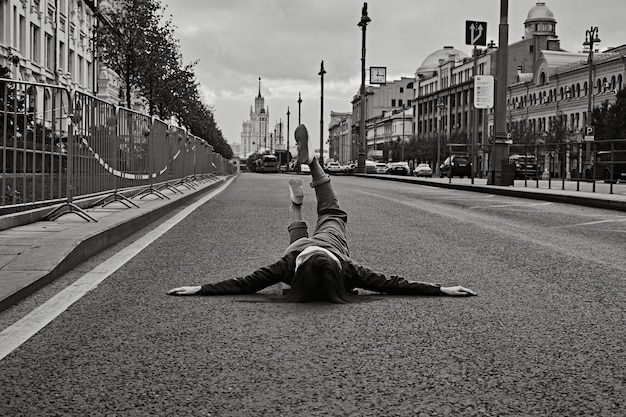 Frau liegt auf einer leeren Asphaltstraße mit erhobenen Beinen.