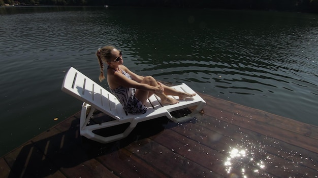Frau liegt auf einer Sonnenliege mit Sonnenbrille und einem Boho-Seidenschal Mädchen ruht auf einem Flutholz-Unterwasserpier Der Bürgersteig ist mit Wasser im See bedeckt
