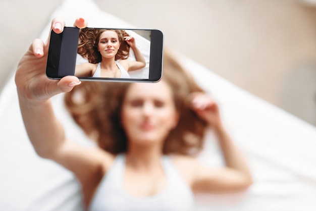 Frau liegt im Bett und macht Selfie