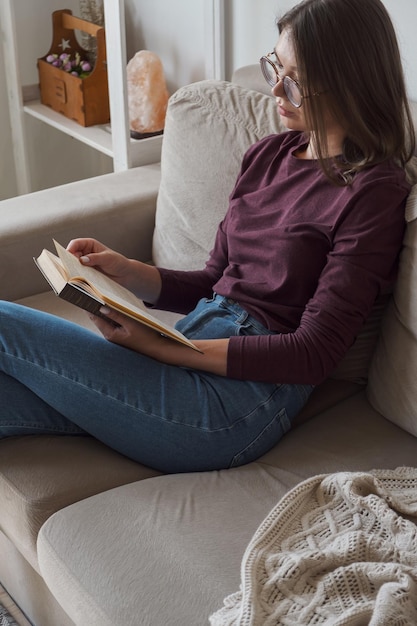 Frau liest ein Buch, das zu Hause auf dem Sofa sitzt