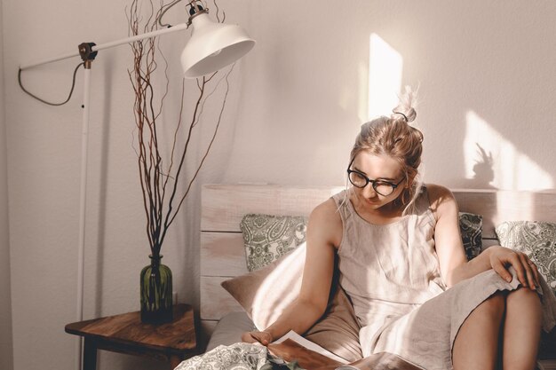 Foto frau liest ein buch, während sie zu hause auf dem bett sitzt