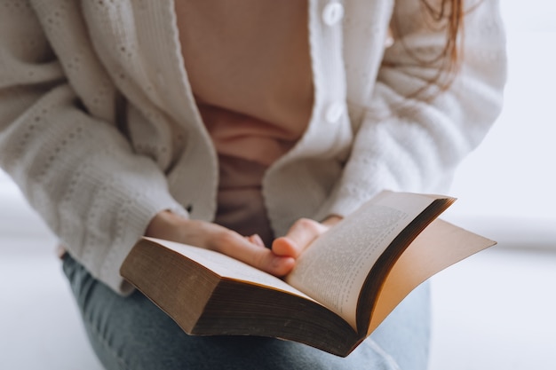 Frau liest tagsüber zu Hause am Fenster ein Buch.