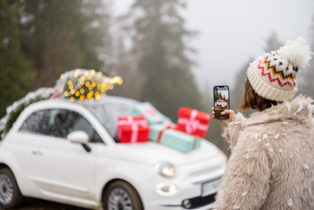 Frau macht am Telefon ein Foto von einem schönen Auto, das für Winterferien dekoriert ist