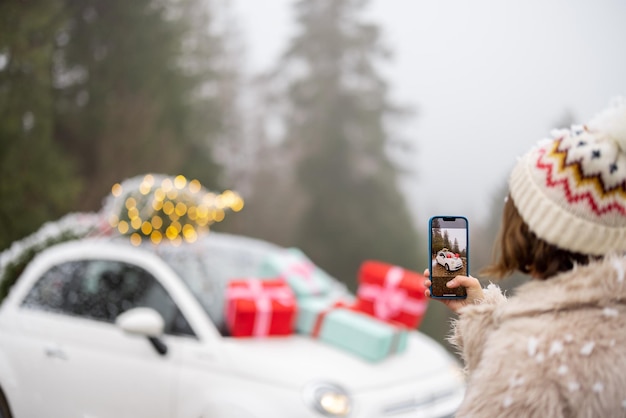 Frau macht am Telefon ein Foto von einem schönen Auto, das für Winterferien dekoriert ist