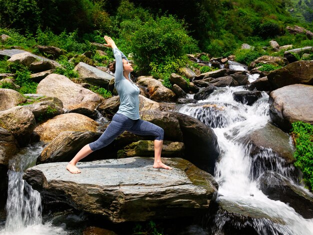 Foto frau macht ashtanga vinyasa yoga asana virabhadrasana 1 krieger pose bei einem wasserfall