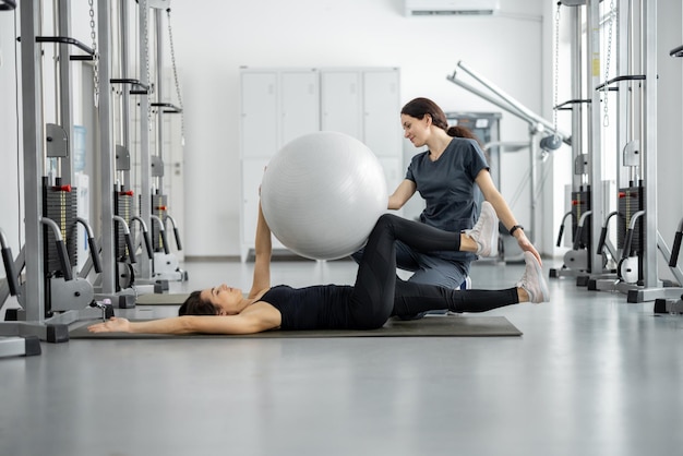 Frau macht Übungen mit Fitnessball mit Rehabilitationsspezialist im Fitnessstudio