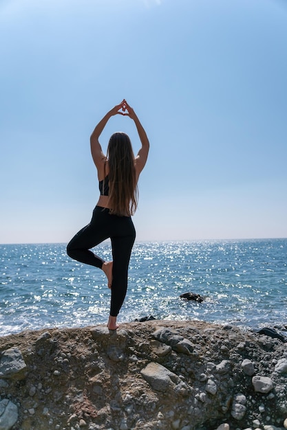 Frau macht Herz mit den Händen am Strand Junge Frau mit langen Haaren Fitnesstrainer dehnen sich vor Pilates auf einer Yogamatte in der Nähe des Meeres an einem sonnigen Tag Fitness-Yoga-Routine-Konzept für Frauen