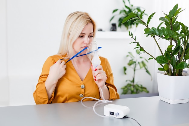 Frau macht Inhalationsvernebler zu Hause. Halten Sie einen Maskenvernebler und inhalieren Sie Dämpfe, um das Medikament in Ihren lungenkranken Patienten zu sprühen. Selbstbehandlung der Atemwege mit Inhalationsvernebler