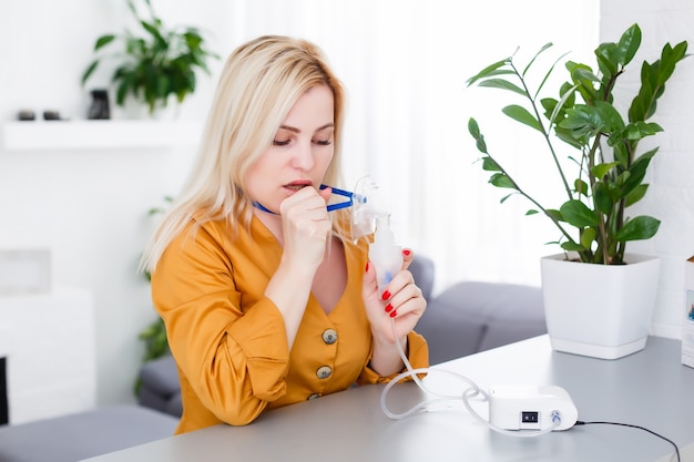 Frau macht Inhalationsvernebler zu Hause. Halten Sie einen Maskenvernebler und inhalieren Sie Dämpfe, um das Medikament in Ihren lungenkranken Patienten zu sprühen. Selbstbehandlung der Atemwege mit Inhalationsvernebler