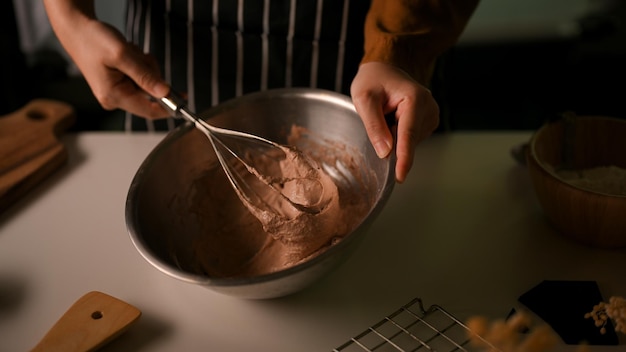 Frau macht Kekse in der Küche mit Schneebesen, um Schokoladenplätzchenteig zu mischen und zuzubereiten