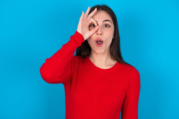 Frau macht ok Geste schockiert mit überraschtem Gesicht Auge, das durch die Finger schaut Unglaublich