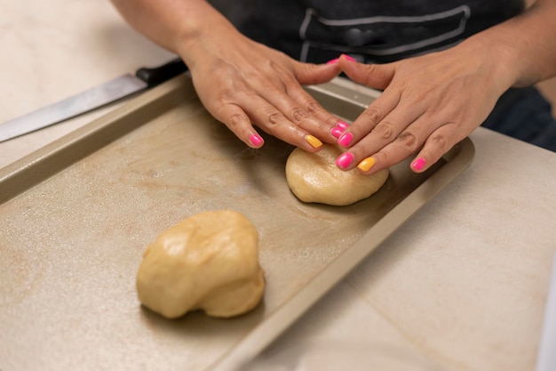 Frau macht Pan de Muerto zu Hause und arrangiert den Teig auf einem Backblech