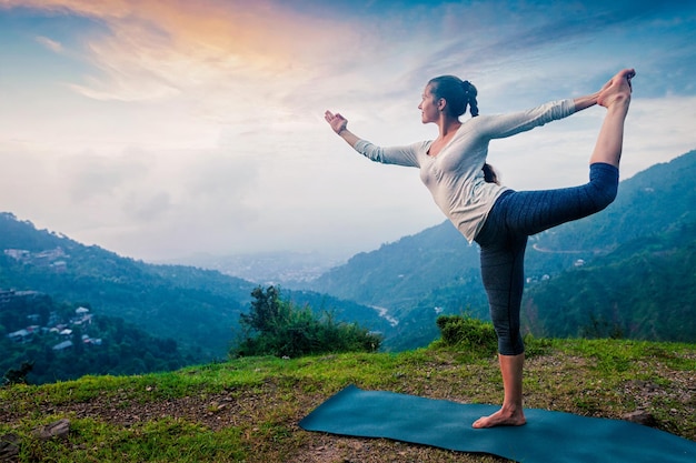 Frau macht Yoga-Asana natarajasana im Freien am Wasserfall