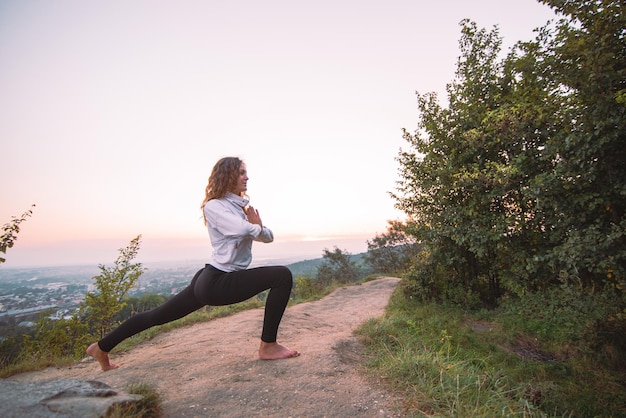 Frau macht Yoga-Übungen oben auf dem Hügel bei Sonnenaufgang