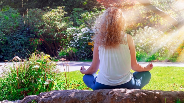 Foto frau macht yoga, während sie gegen pflanzen sitzt