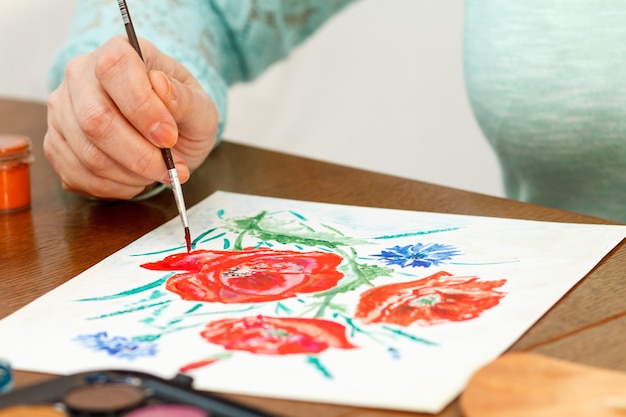 Frau malt Mohnblumen auf einem weißen Blatt Papier