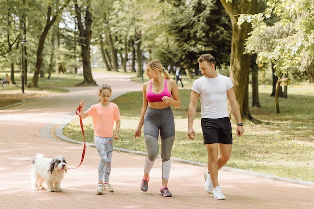 Frau, Mann und kleines Mädchen joggen mit ihrem Hund im Park