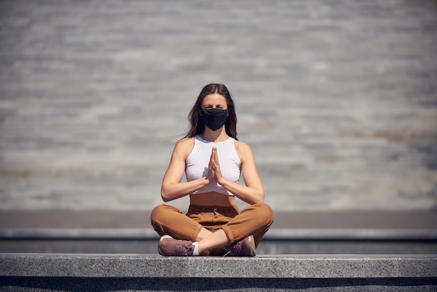 Frau meditiert an einem leeren öffentlichen Ort in einer schwarzen Maske. Epidemie des Coronavirus-Konzeptfotos