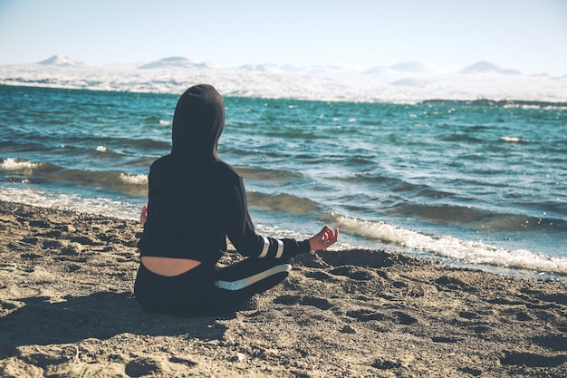 Frau meditiert in einer Lotushaltung am Strand sitzend