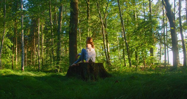 Frau meditiert Zen-Yoga-Meditationspraxis in der Natur. Rückansicht eines Yoga-Mädchens, das auf einem Baumstumpf sitzt