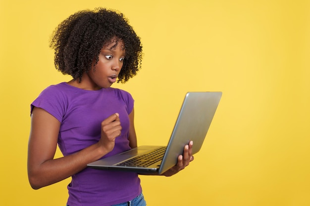 Frau mit Afro-Haaren, die einen Laptop mit schockiertem Ausdruck anschaut