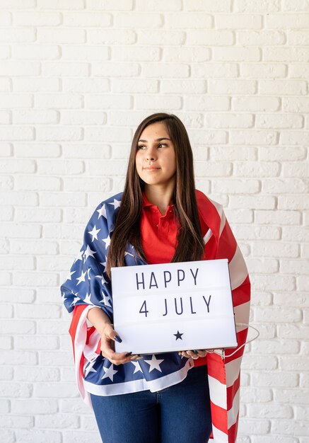 Frau mit amerikanischer Flagge, die Leuchtkasten mit Worten glücklich 4. Juli hält